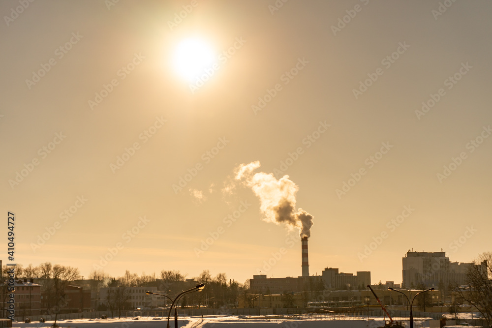Cityscape on sunset. From the boiler room tube goes white steam, smoke into the sky. Industrial zone in big city. Heating in winter Cityscape on sunset. From the boiler room tube goes white steam, smoke into the sky. Industrial zone in big city. Heating in winter