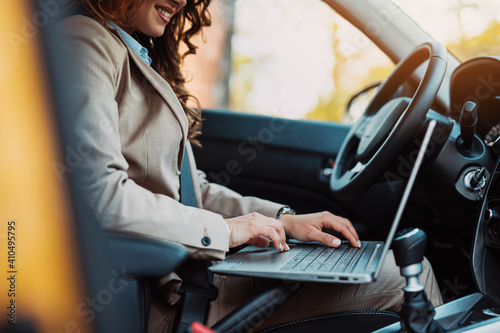 Beautiful young businesswoman driving car and using laptop.