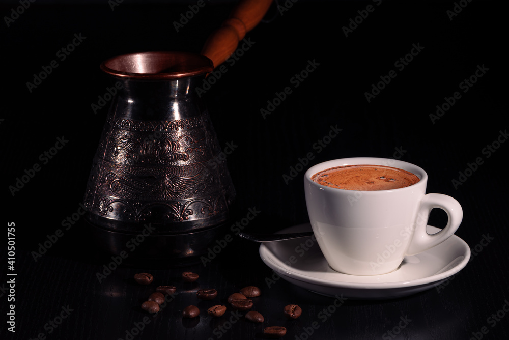 White cup of coffee, copper cezve and coffee beans on black wooden table. Low key. Copy space.