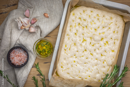 The process of making focaccia of natural sourdough with rosemary and garlic. Whole grain dough before baking on a wooden background. Artisan