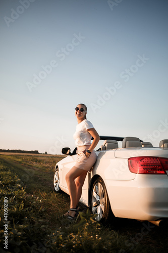A beautiful young woman of European appearance on the face of sunglasses, she stands near her white convertible. Successful woman businesswoman and her white car. © Дмитрий Ткачук