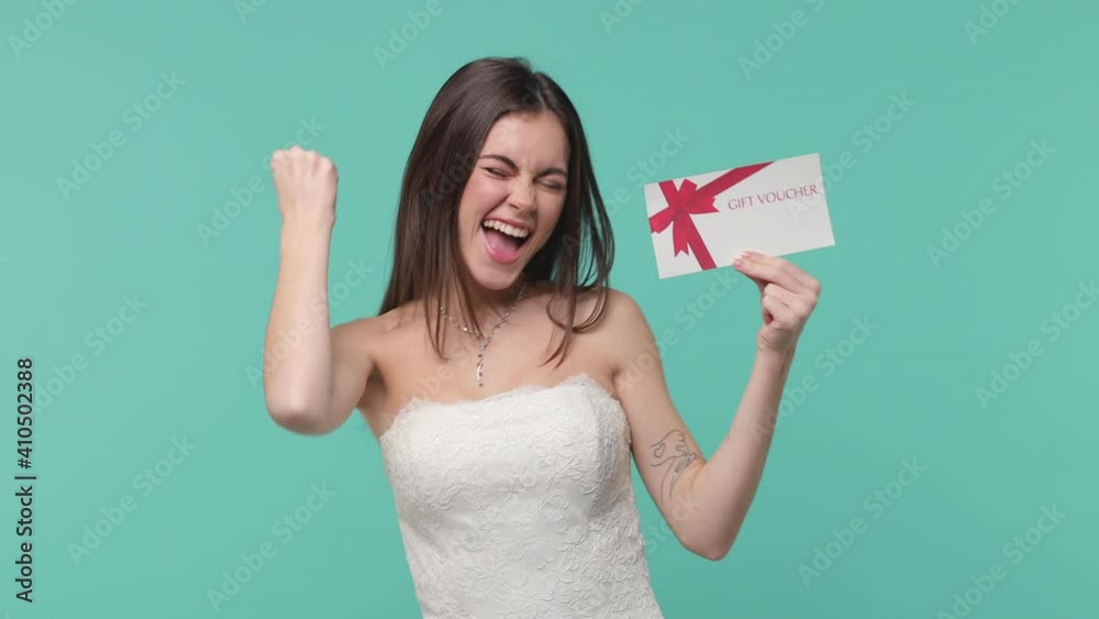 Surprised amazed bride young woman 20s in white wedding dress isolated on blue turquoise color background studio. Wedding concept. Point index finger on gift certificate doing winner gesture say yes Surprised amazed bride young woman 20s in white wedding dress isolated on blue turquoise color background studio. Wedding concept. Point index finger on gift certificate doing winner gesture say yes