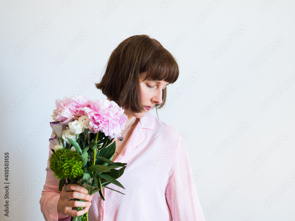 Young woman holding beautiful pastel peony bouquet on light gray background