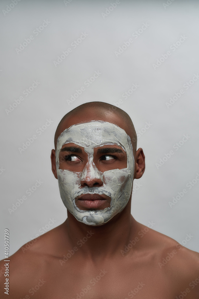 Handsome young african american man looking aside, using facial blackhead removal mask, posing isolated over gray background
