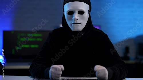 Nervous stressed unrecognizable hacker in black clothes and anonymous mask beating table with fists. Anxious man failing in hacking or coding online virus. photo