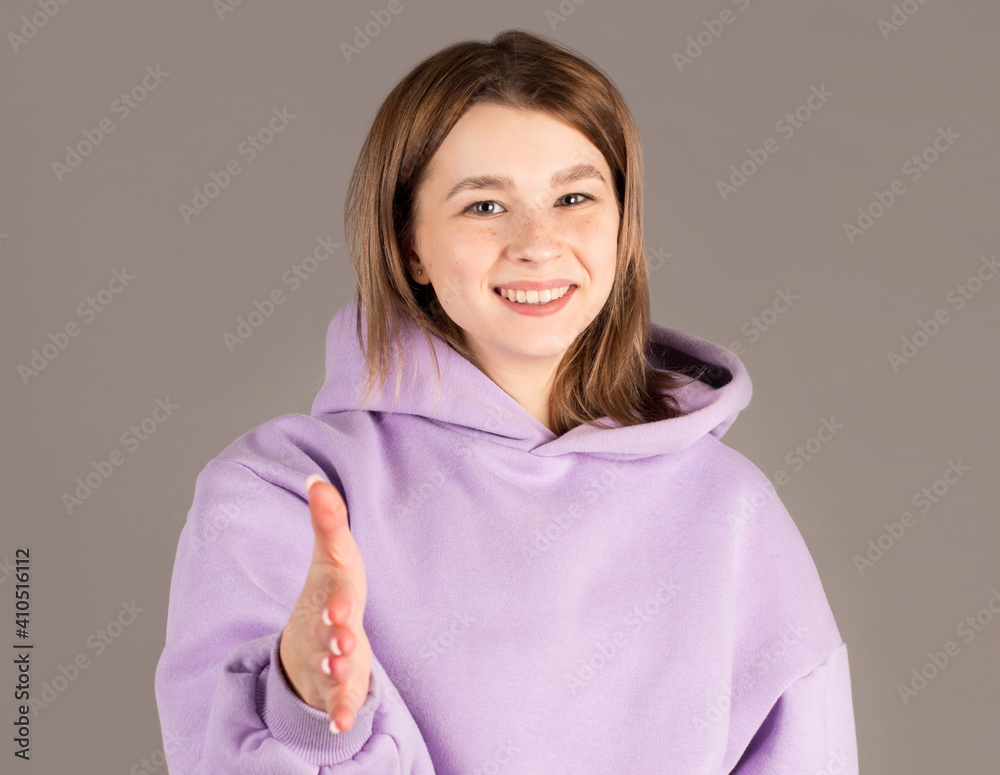 Young woman in purple sweater reaching for shake hand to greet someone, isolated on gray background. Young woman in purple sweater reaching for shake hand to greet someone, isolated on gray background.
