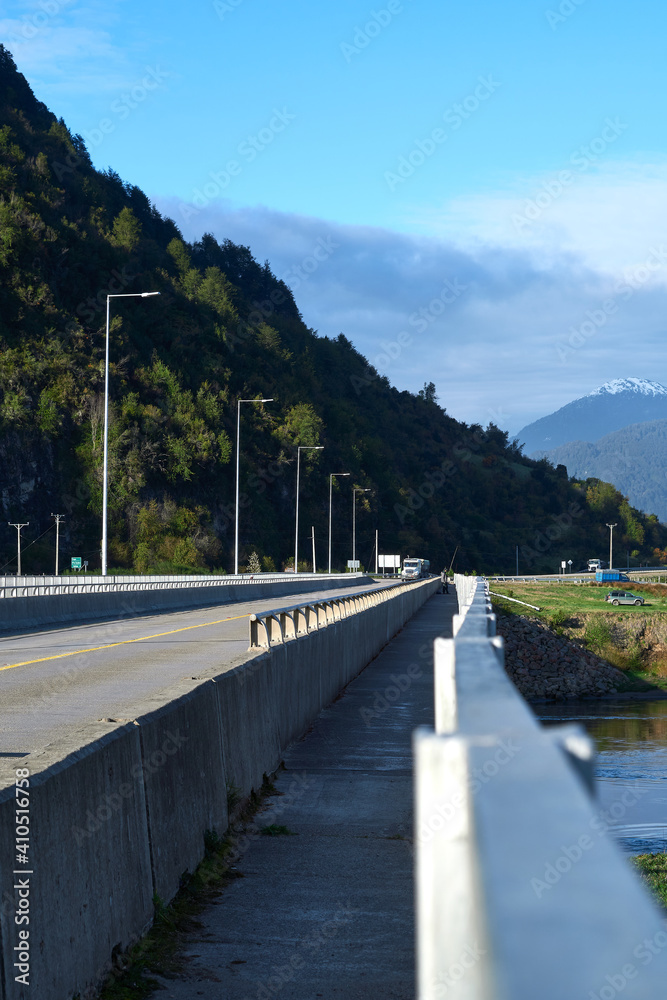 Obraz premium Narrow sidewalk of a bridge over a river in the countryside.