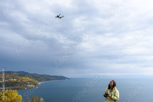 Beautiful young woman having fun with a mini drone outdoors. The girl stands against the autumn forest background