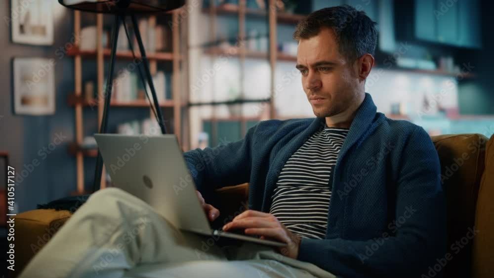 Handsome Caucasian Man Working on Laptop Computer while Sitting on a Sofa in Stylish Cozy Living Room. Freelancer Working From Home. Browsing Internet, Using Social Networks, Having Fun in Flat.