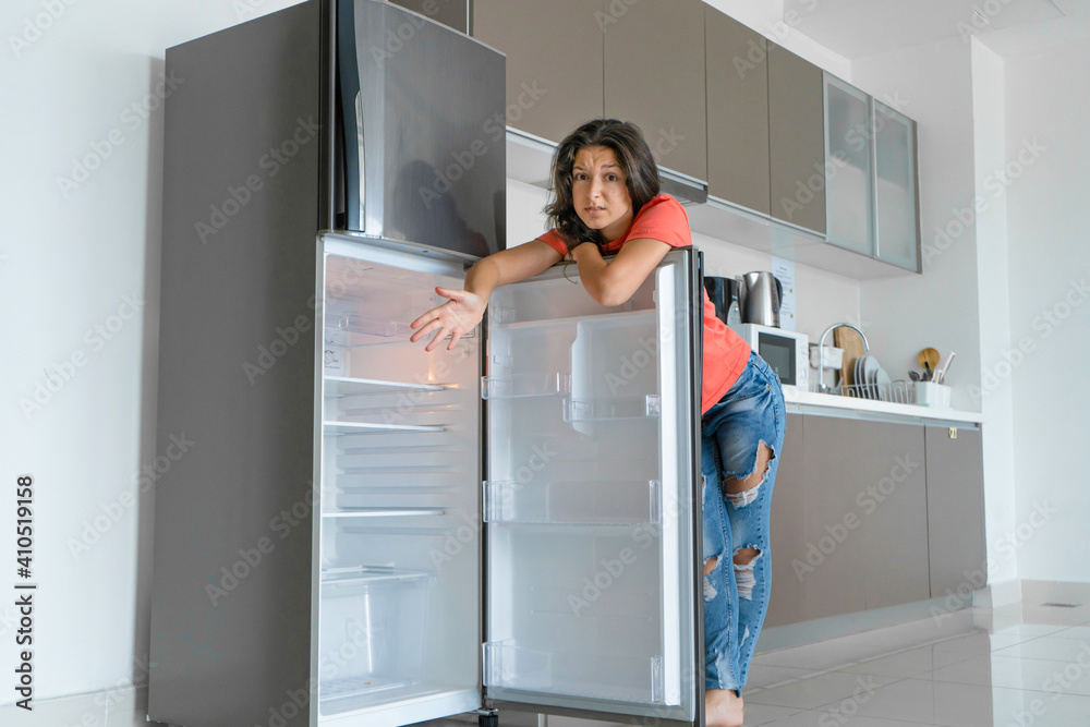 The girl is surprised at the empty refrigerator. Lack of food. Food delivery The girl is surprised at the empty refrigerator. Lack of food. Food delivery