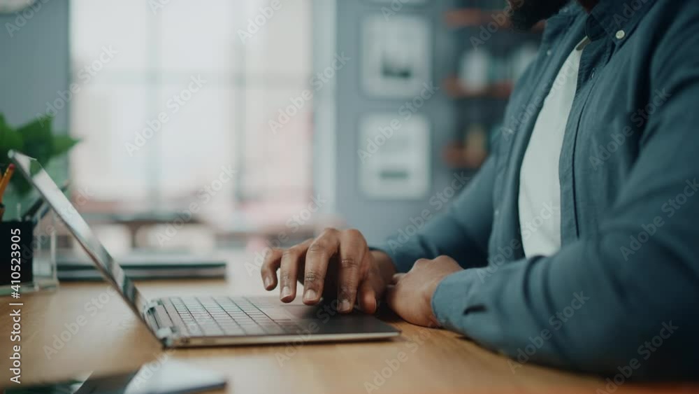 Close Up on Hands of a Black African American Man Working on Laptop Computer while Sitting Behind Desk in Cozy Living Room