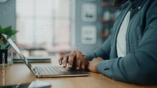 Close Up on Hands of a Black African American Man Working on Laptop Computer while Sitting Behind Desk in Cozy Living Room photo