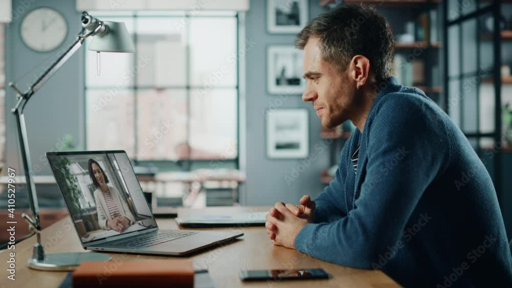 Handsome Caucasian Man Having a Video Call on Laptop Computer while Sitting Behind Desk in Living Room. Freelancer Working From Home and Talking to Colleagues and Clients Over the Internet. Handsome Caucasian Man Having a Video Call on Laptop Computer while Sitting Behind Desk in Living Room. Freelancer Working From Home and Talking to Colleagues and Clients Over the Internet.