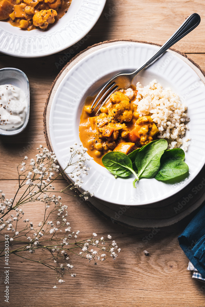 Chickpea and cauliflower vegetarian curry with brown rice and spinach on a wooden table.