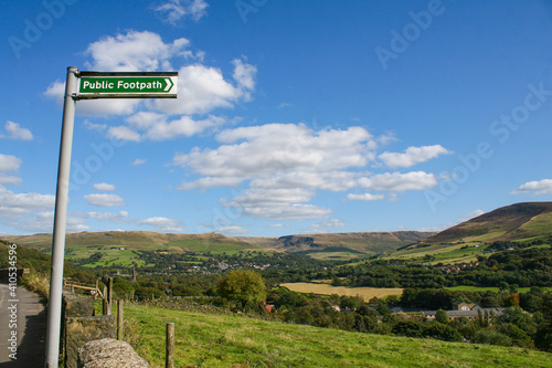 Mossley, England - A view of rolling hills on the outskirts of Mossley England, under a sign that says "public footpath", under an idyllic blue sky. Image has copy space.
