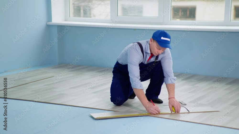 foreman measures the length and width of the board with a tape measure and marks with a pencil before laying the laminate, renovation in a new house or apartment foreman measures the length and width of the board with a tape measure and marks with a pencil before laying the laminate, renovation in a new house or apartment