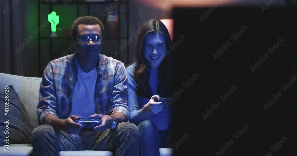 Happy multinational couple playing video game on console sitting at home in evening. Two people have fun. Happy multinational couple playing video game on console sitting at home in evening. Two people have fun.