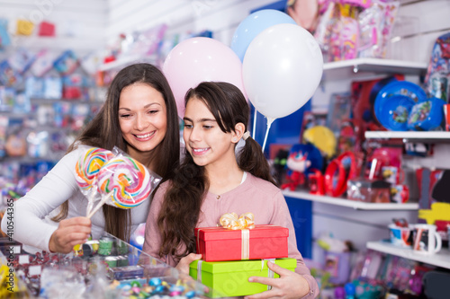 Happy woman with daughter holding candies and gifts in candy shop