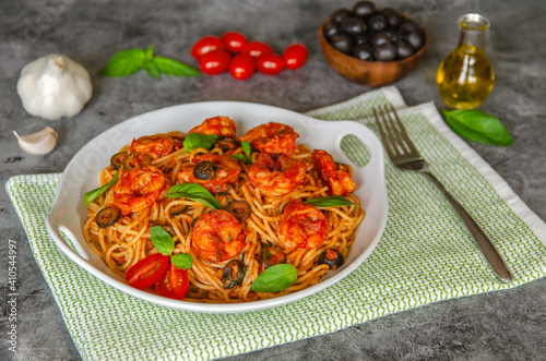 Pasta in tomato sauce with shrimps, olives, basil and garlic on a beautiful plate.