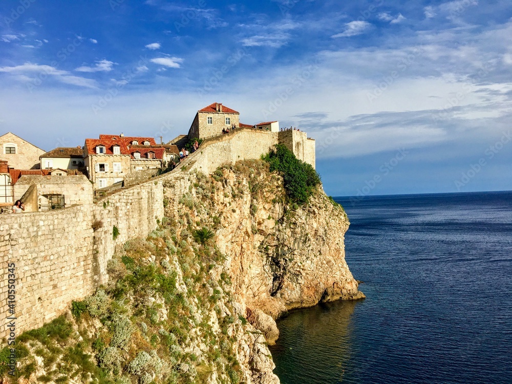 A view of a section of the walls of Dubrovnik facing outwards to the Adriatic Sea.  People are standing in the distance admiring the view.