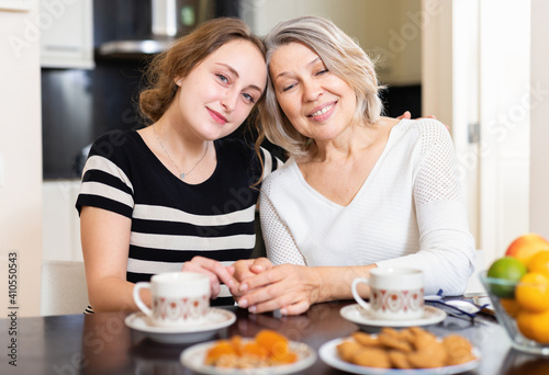 Mature mother and adult daughter enjoying conversation over cup of coffee at home