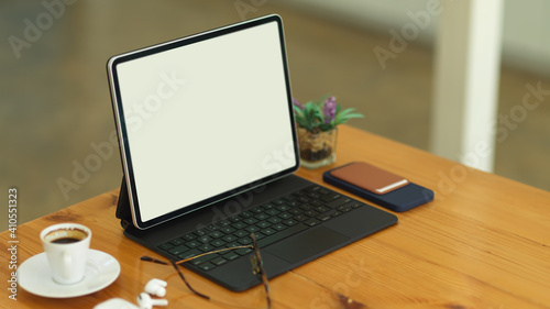 Cropped shot of wooden table with tablet, keyboard, eyeglasses, accessories and cup