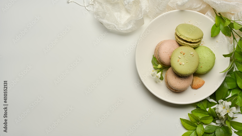 White table with a plate of French colourful macarons, copy space decorated with flower and leaves White table with a plate of French colourful macarons, copy space decorated with flower and leaves