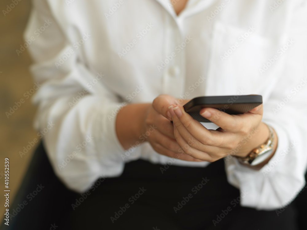 Female hand using smartphone while sitting in office room Female hand using smartphone while sitting in office room