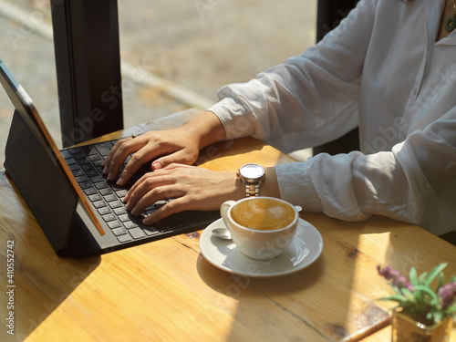 Female hands typing on tablet keyboard on wooden table with coffee cup in cafe