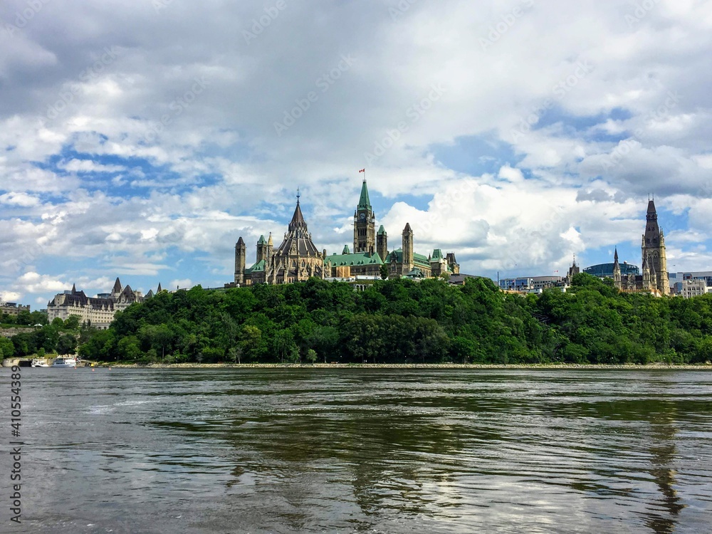 An amazing view of parliament hill surrounded by green forest and chateau laurier from the perspective of a tour boat on the Ottawa river.  This is beautiful view of the cityscape on a nice summer day