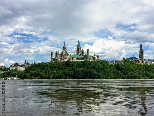 An amazing view of parliament hill surrounded by green forest and chateau laurier from the perspective of a tour boat on the Ottawa river. This is beautiful view of the cityscape on a nice summer day