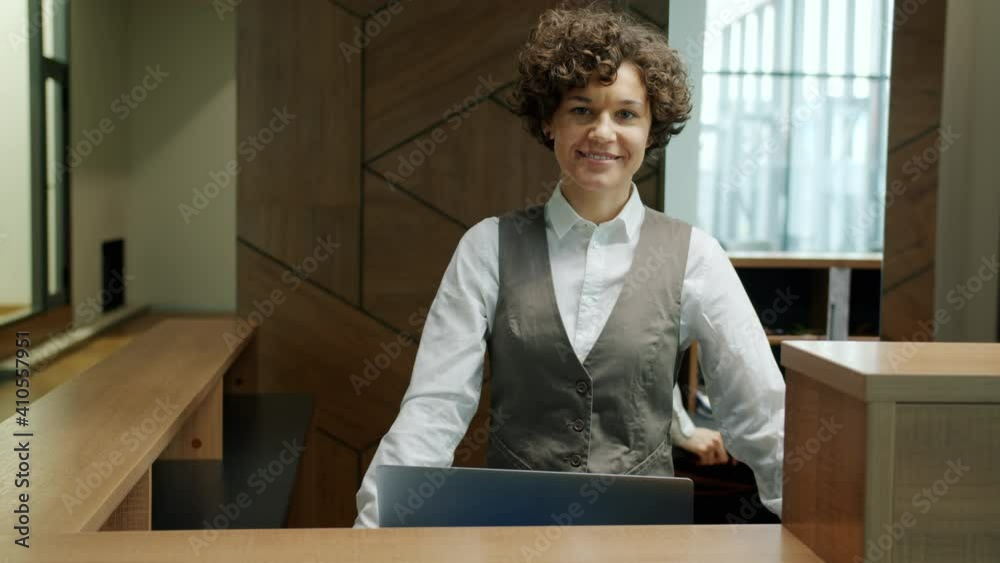 Portrait of attractive young woman in uniform standing at reception desk alone smiling looking at camera. Business locations and professions concept.