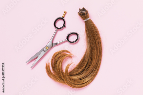 Foto The cut off strand of female children's hair of light brown color and scissors on a pink background