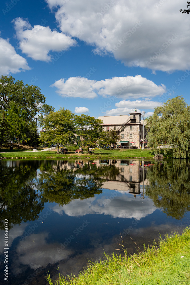Stewart Park, a view of the willow trees and old stone house surrounded by trees, reflected on pond in summer. Perth, Ontario, Canada.