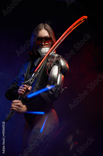Atmospheric portrait of a beautiful female assassin posing in dark background with smoke. Armed with glowing sword military woman with sunglasses and implant.