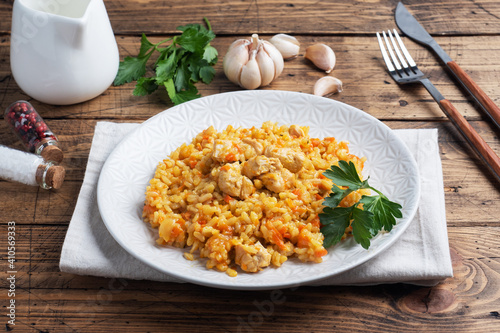 Delicious Asian pilaf, stewed rice with vegetables and chicken on a plate. Wooden rustic background.