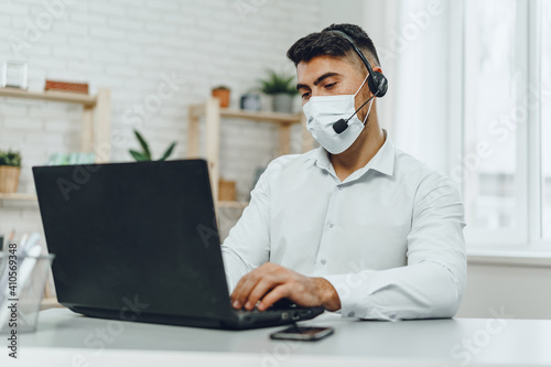 Young businessman sitting at his working desk with medical mask on