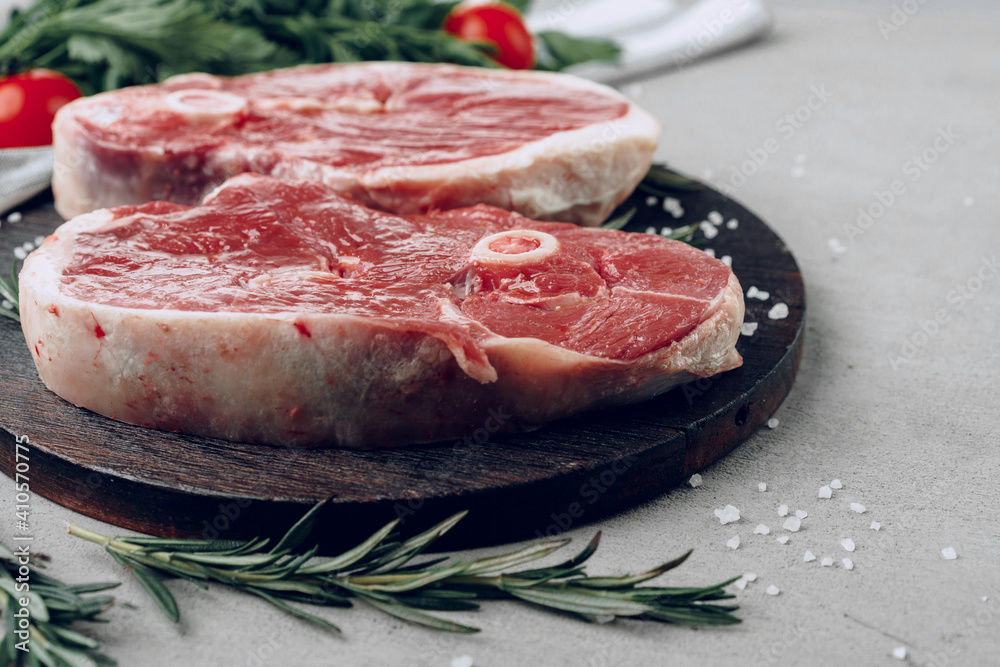 Raw rib-eye beef steak on wooden cutting board on gray background