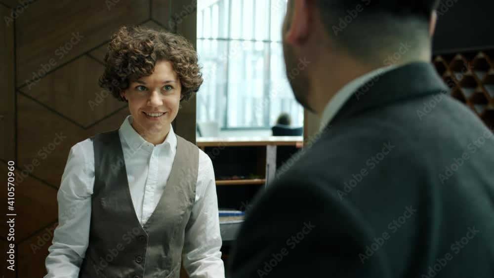 Hotel administrator in uniform is greeting middle-aged businessman giving key card standing at desk together. Travelling and accommodation concept.