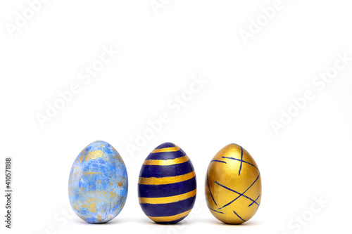 Three easter eggs trendy colored classic blue, white and golden decorated on white table. Happy Easter card with copy space for text. Minimal style.
