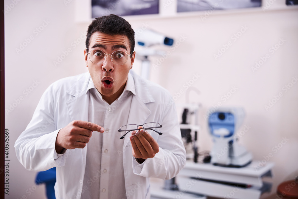 Surprised optician in a lab coat holding semi-rimless spectacles Surprised optician in a lab coat holding semi-rimless spectacles