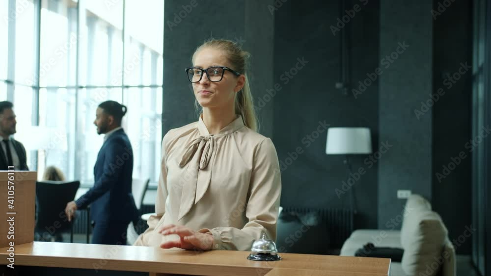 Young woman is arriving at hotel ringing bell at reception desk talking to administrator getting key card then walking to room. People and travelling concept.
