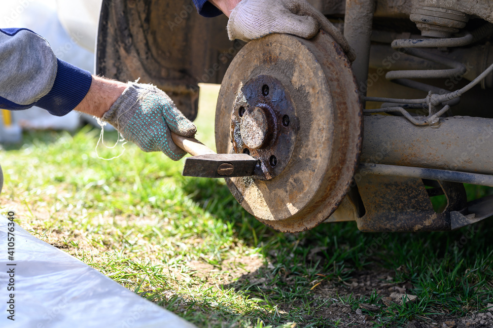 men's gloved hands repair of car drum brake himself. disassembles a jammed disk with a hammer. repair of broken car drum brake disassembled outdoor