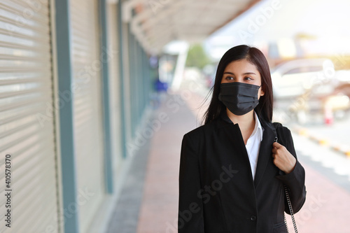 Young asian business woman in business black suit with protect mask for healthcare walking on street public outdoor and looking way. New normal and social distancing concept