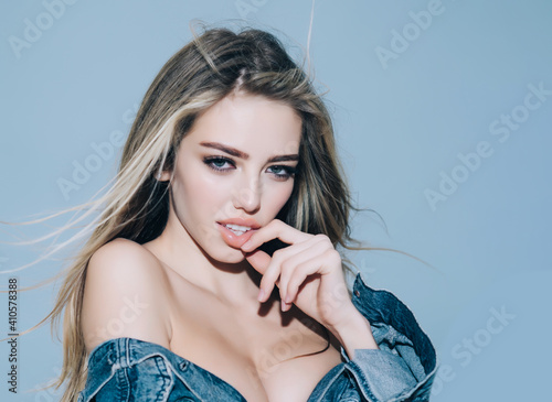 Beautiful female face with perfect skin. Fashion photo of a beautiful young woman in a pretty jeans clothes posing over blue background. Fashion photo.