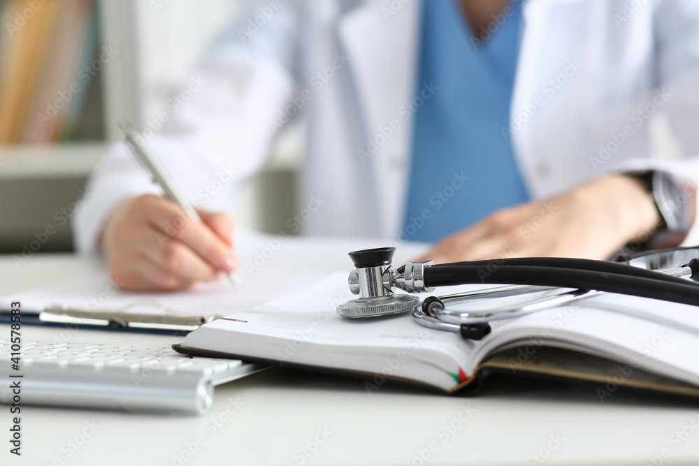 Stethoscope head lying on medical forms closeup while medicine doctor working in background. Patient history list, visit check, 911, medical calculation and statistics, healthy lifestyle concept Stethoscope head lying on medical forms closeup while medicine doctor working in background. Patient history list, visit check, 911, medical calculation and statistics, healthy lifestyle concept