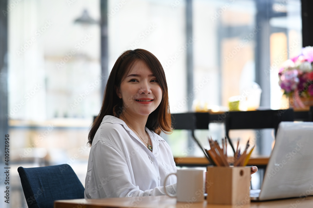 Cheerful young female employee sitting at her workspace and smiling to camera. Cheerful young female employee sitting at her workspace and smiling to camera.