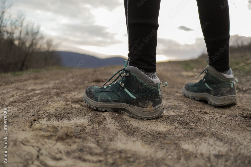Naklejka premium Trekking boots in mud with sunset sky background