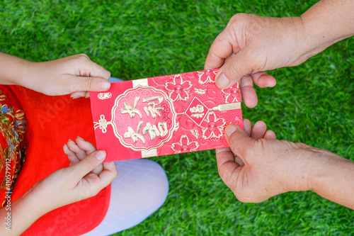 We Chinese always wish people Happy Chinese New Year Senior women hands giving red packet to little girl hands on the grass/, Chinese New Year festival concept