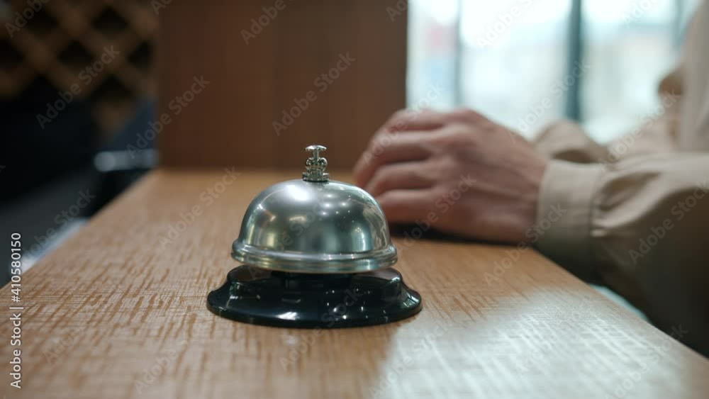 Close-up of female hand ringing reception desk bell then taking key card during check-in in hotel lobby. Travelling and accommodation concept.